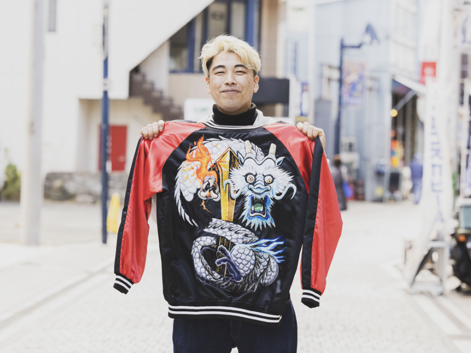 龍のスカジャンを手にするドブ板コーバスタジオ店主の山上大輔さん